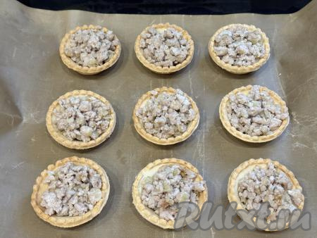 Тарталетки поставить на противень, застеленный ковриком (или пергаментом). Разложить фарш по тарталеткам, заполняя их полностью.&nbsp;