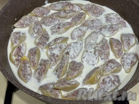 Влить сливочный соус в сковороду к ракушкам с фаршем. Соус должен практически полностью покрывать макароны. Если необходимо, добавьте ещё немного воды, в этом случае соус нужно будет немного подсолить. Сковороду с фаршированными ракушками поставить на огонь выше среднего.&nbsp;