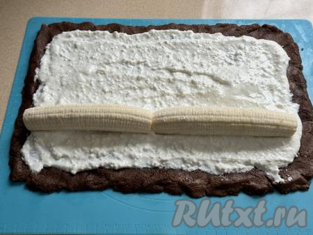Очистить 2 банана. Поверх творожной начинки ближе к краю одной из длинных сторон пласта выложить в один ряд 2 банана, как на фото. Если необходимо, отрезать кончики бананов, чтобы они не выходили за края творожного слоя.