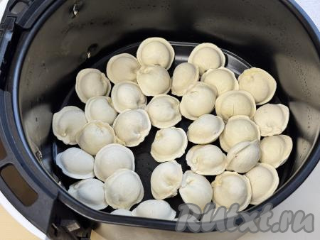 Чашу аэрогриля без решётки немного смазать растительным маслом, выложить замороженные пельмени в один слой.