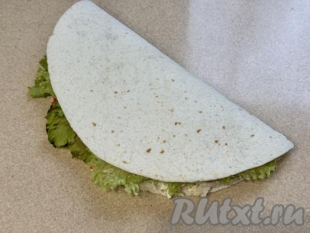 Половину тортильи с начинкой накрыть чистой половиной тортильи.