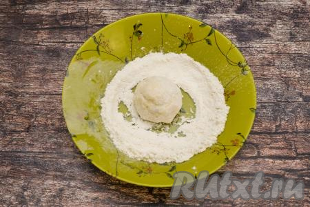 В отдельную глубокую тарелку насыпать примерно 1,5 столовых ложки муки. Зрительно разделить творожное тесто на 6 равных частей (именно столько сырников мы и будем готовить в духовке). Смачивая руки водой, из каждой части теста сформировать круглый сырник, сразу поместить его в тарелку с мукой и обвалять со всех сторон в муке. Творожное тесто для сырников липкое, поэтому обязательно перед формовкой сырников смачивайте руки водой, тогда и работать с тестом будет проще, и обваливаться в муке сырники будут лучше.