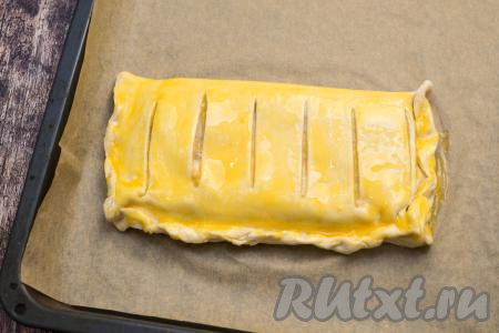 Отложенный ранее яичный желток взболтать вилкой до однородности, а затем смазать им поверхность пирога.
