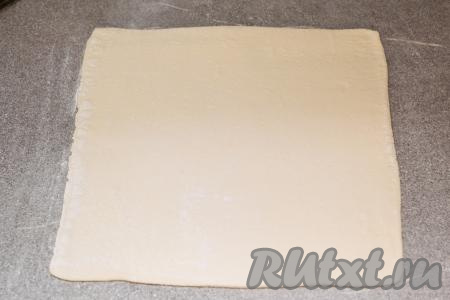 Размороженное слоёное тесто выложить на припылённый мукой стол и раскатать в квадрат со стороной примерно 25 сантиметров. Толщина раскатанного теста должна быть ориентировочно 2,5-3 миллиметра.