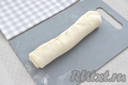 На слегка присыпанной мукой поверхности размороженный пласт слоёного теста, не раскатывая, сворачиваем в рулет. Край теста прижимаем плотно к рулету, тем самым тщательно закрепляя край.