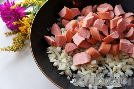 Добавить к луку нарезанные сосиски, перемешать, готовить ещё 2 минуты.