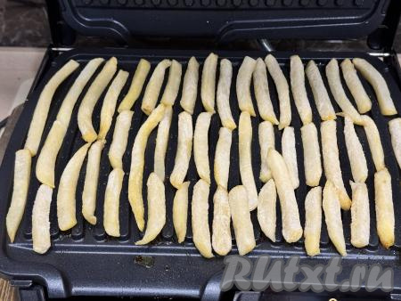 Створки электрогриля смазать растительным маслом. Выложить нарезанный свежий картофель (или замороженную картошку фри) на нижнюю створку электрогриля в один слой.&nbsp;