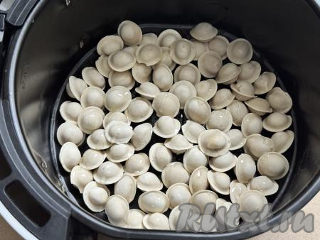 В чашу аэрогриля, убрав из неё решётку, выложить пельмени. Сбрызнуть пельмени маслом, выставить температуру 180 градусов, время - 10 минут. Отправить чашу с пельменями в аэрогриль.