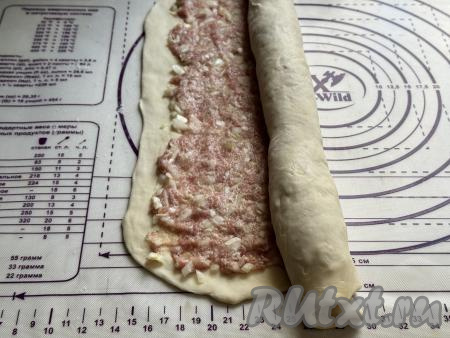 На раскатанное теста, отступая от краёв теста по 1 сантиметру, равномерно выложить начинку из капусты и фарша. Затем свернуть тесто с начинкой в рулет.