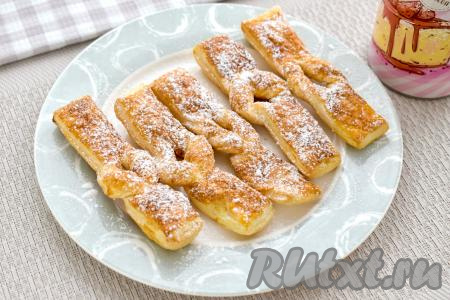 Готовый хворост перекладываем из чаши аэрогриля на тарелку. Постепенно готовим в аэрогриле оставшиеся заготовки хвороста из слоёного теста, не забывая перед выпечкой смазывать их яйцом и посыпать сахаром. Остывший хворост присыпаем сахарной пудрой.&nbsp;