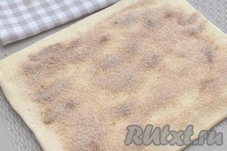 Поверхность раскатанного теста равномерно посыпаем смесью сахара и корицы, отступая от краёв теста по 1 сантиметру.