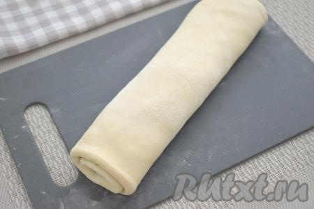 Начиная с более узкой стороны пласта, сворачиваем тесто с начинкой в неплотный рулет. Край теста немного смазываем водой и прижимаем к сформированному рулету. Выкладываем рулет швом вниз.