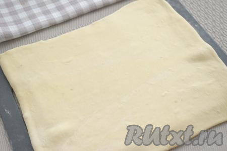 Слегка присыпаем стол мукой, выкладываем размороженное слоёное тесто, раскатываем его в прямоугольный пласт размером 22 сантиметра на 25 сантиметров.