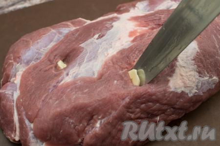 В куске свинины со всех сторон сделать острым ножом надрезы. Вставить в надрезы кусочки чеснока.