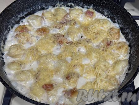 Довести сливки до кипения, сразу убавить огонь до минимума и тушить 8 минут под крышкой, в течение этого времени пельмени с беконом нужно будет несколько раз аккуратно перемешать, чтобы они равномерно протушились в соусе. Затем присыпать пельмени сыром, натёртым на крупной тёрке и, накрыв крышкой, снять сковороду с огня.