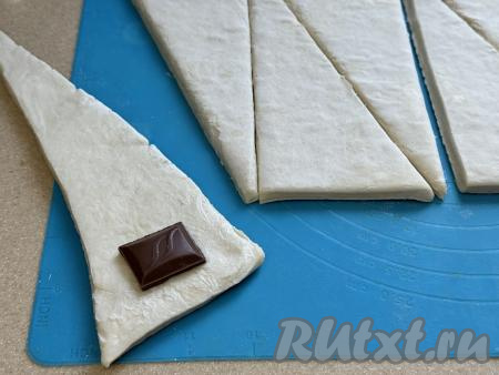 Ближе к основанию треугольника, отступая от краёв теста по 1 сантиметру, выложить 1 дольку шоколада.
