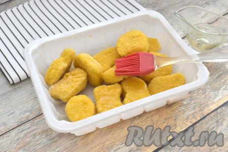 Открываем упаковку готовых замороженных наггетсов, размораживать их не нужно. Замороженные наггетсы немного смазываем с двух сторон растительным маслом. Благодаря маслу, в процессе приготовления в аэрогриле на наггетсах получится более хрустящая корочка, при этом внутри кусочки мяса останутся мягкими и сочными.