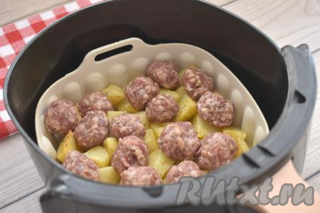 Через 20 минут от начала приготовления открываем аэрогриль, достаём чашу, картофель перемешиваем. Поверх картошки в один слой раскладываем сформированные мясные фрикадельки и отправляем чашу в аэрогриль.