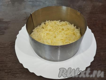 Этот слоёный салат лучше всего формировать с помощью кулинарного кольца (я взяла кольцо диаметром 14 сантиметров), поставив его на плоскую тарелку. Первым слоем выкладываем картофель, натёртый на крупной тёрке. Немного утрамбовываем его вилкой.