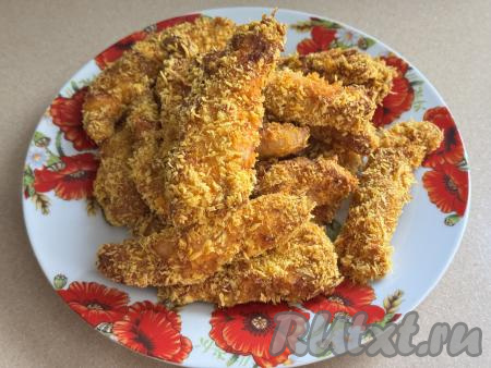 Готовые стрипсы переложить из чаши аэрогриля на плоскую тарелку. Постепенно запечь оставшиеся полоски куриного мяса в панировке.