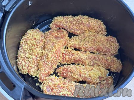 Решётку в чаше аэрогриля смазать растительным маслом (или застелить пергаментом, фольгой), выложить в один слой подготовленные куриные стрипсы в хрустящей панировке. Отправить чашу в аэрогриль.