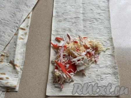 Разрезать лаваш на 8 полосок. Начинку из крабовых палочек и сыра тоже визуально разделить на 8 частей. Ближе к одному краю лаваша, отступая от краёв полоски, выложить часть начинки в виде треугольника, как на фото.