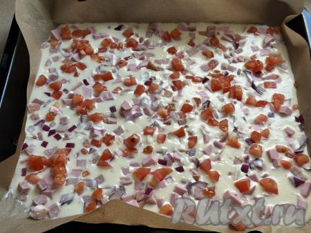 Затем по тесту равномерно разложить кубики колбасы, нарезанные лук и помидоры.