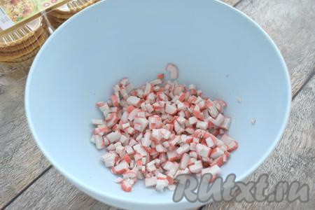 Если крабовые палочки заморожены, их нужно разморозить при комнатной температуре. Крабовые палочки вынимаем из упаковки, нарезаем на мелкие кубики, выкладываем в миску.