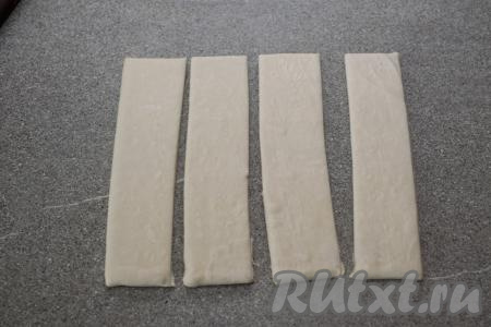 На слегка присыпанную мукой поверхность выложить разморозившееся слоёное тесто. Не раскатывая его, разрезать острым ножом на 4 одинаковых полоски.&nbsp;