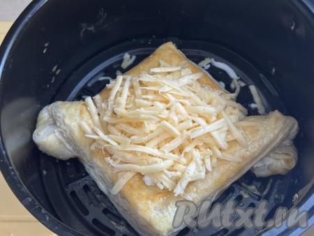 Сыр натереть на крупной тёрке. По прошествии 15 минут достать чашу из аэрогриля, выложить в середину хачапури половину натёртого сыра. Отправить хачапури из слоёного теста с сыром в аэрогриль, выпекать 10 минут при температуре 150 градусов.