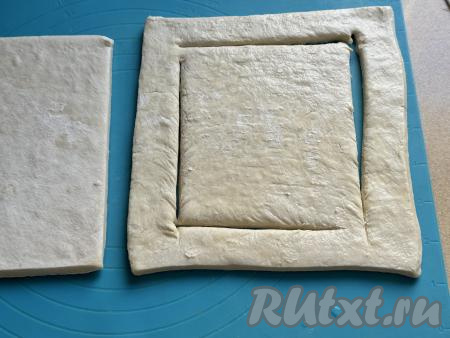 Размороженное тесто выложить на рабочую поверхность, припылённую мукой. Раскатывать тесто не нужно. Взять один пласт теста, отступая от краёв по 1,5 сантиметра, на двух противоположных углах сделать г-образные разрезы, немного не доходя до двух оставшихся углов, как на фото.