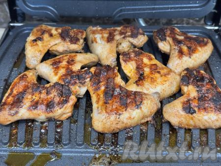 Перевернуть куриные крылышки и готовить в электрогриле ещё 10 минут.