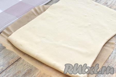 Для того чтобы испечь слоёный пирог в аэрогриле, нам понадобится специальный вкладыш из пергамента, который мы будем помещать в дальнейшем в чашу аэрогриля, или кусок пергамента, вырезанный по размеру чаши аэрогриля. Присыпаем стол немного мукой, раскатываем размороженный пласт слоёного теста в прямоугольник, ориентируясь на размер чаши аэрогриля. Меньшая сторона прямоугольника должна помешаться в чашу аэрогриля, а большая сторона будет примерно вдвое длиннее. Раскатанное тесто помещаем на пергамент, которым в дальнейшем будем застилать чашу аэрогриля, как на фото.