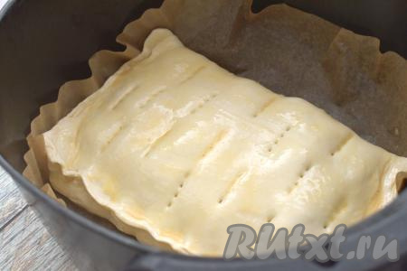 Начинку накрываем свободной стороной теста, края пирога плотно скрепляем руками. На поверхности пирога делаем проколы вилкой для выхода пара во время выпечки. Заготовку пирога из слоёного теста с яблоками вместе с пергаментом помещаем в чашу аэрогриля. В небольшой ёмкости взбиваем яйцо вилкой до однородности, получившейся яичной смесью смазываем поверхность пирога. Чашу с заготовкой пирога отправляем в аэрогриль.