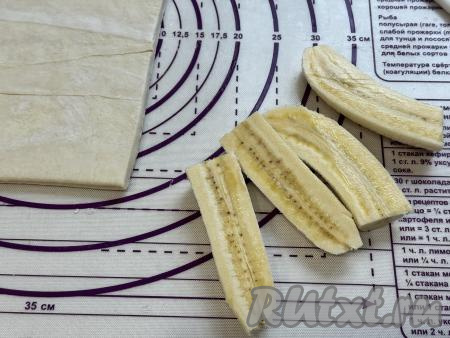 Размороженный пласт слоёного теста выложить на рабочую поверхность. Бананы очистить от кожуры. Разрезать каждый банан вначале в длину пополам, а затем каждую половину банана разрезать ещё на 2 части. В результате каждый банан будет разрезан на 4 части.