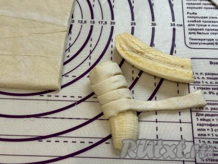 Взять одну полоску теста, обернуть её вокруг кусочка банана, слегка растягивая тесто, как на фото. При желании можно наматывать полоску на банан, накладывая тесто слегка внахлёст. Постепенно завернуть в полоски из слоёного теста все кусочки бананов.&nbsp;