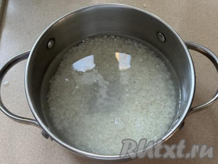 Прежде всего нужно сварить рис. Для этого рис нужно выложить в сито, хорошо промыть под проточной водой, убирая с риса крахмал. Лишней воде дать с риса стечь. В кастрюле вскипятить воду, подсолить, выложить подготовленный рис, перемешать, дать закипеть, уменьшить огонь, варить до готовности риса (минут 20-25, рисинки должны стать мягкими, но не переваренными). Сварившийся рис откинуть на сито, оставить на несколько минут, чтобы лишняя вода стекла и рис остыл.