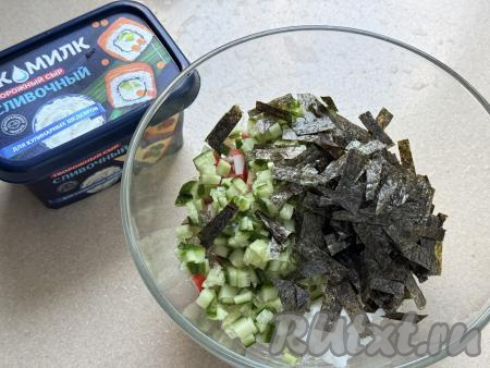 Листы нори нарезать кухонными ножницами на небольшие кусочки и вместе с огурцом выложить в миску с рисом и крабовыми палочками.