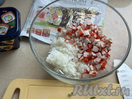 В глубокую миску выложить остывший рис и нарезанные крабовые палочки.