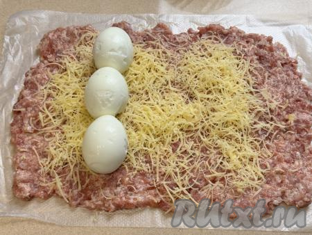 Отступив от узкого пласта фарша, посыпанного сыром, сантиметра 2-3, выложить в ряд варёные яйца, как на фото.&nbsp;