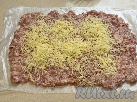 Сыр натереть на мелкой тёрке. Отступая от одного узкого и двух широких краёв пласта из фарша по 1 сантиметру, а от второго узкого пласта - 2 сантиметра, посыпать фарш натёртым сыром.