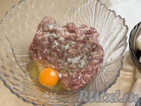 В миску выложить фарш, добавить 1 сырое яйцо, всыпать соль и чёрный молотый перец. Тщательно перемешать фарш.&nbsp;