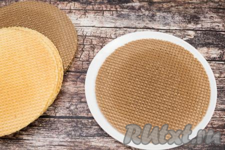 На плоскую тарелку или доску выложить первый вафельный корж. У меня вафельные коржи были двух цветов, поэтому, для того чтобы торт более красиво смотрелся в разрезе, я коржи выкладывала поочерёдно. Перед формированием торта осмотрите все коржи, если есть повреждённые, тогда их используйте в середине торта, а нижним и верхним - должны быть коржи без повреждений.