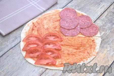 Помидор моем, обсушиваем, нарезаем на тонкие полукружочки. Колбасу нарезаем на тонкие кружочки (или полукружочки). Сыр натираем на крупной тёрке. Визуально делим лепёшку на 4 сегмента. На противоположные сегменты выкладываем половину нарезанной колбасы и половину нарезанных помидоров.