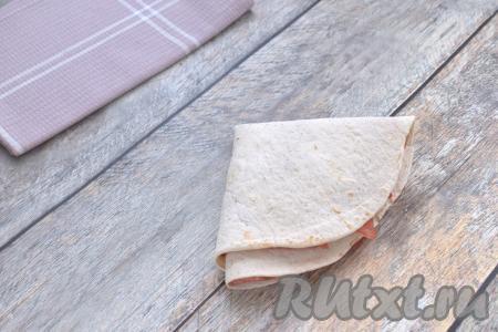 Повторяем сворачивание, в результате получается заготовка из лепёшки "Тортилья" с начинкой из колбасы и сыра в виде треугольника. Аналогично формируем второй треугольник из тортильи и оставшихся помидоров, колбасы и сыра.