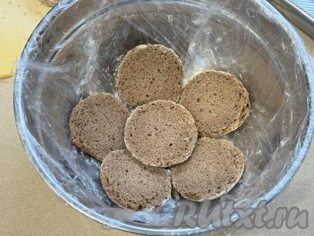 Достаточно объёмную миску (я взяла миску диаметром 18 сантиметров) застелить пищевой плёнкой так, чтобы края плёнки свисали с краёв миски. Дно застеленной миски смазать кремом, выложить несколько половинок пряников, закрывая дно миски, как на фото.&nbsp;