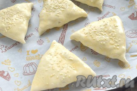 Сформированную самсу из слоёного теста с курицей и грибами выкладываем швом вниз на противень, застеленный пергаментом. Аналогично формируем ещё 4 самсы, тоже выкладываем на застеленный противень на небольшом расстоянии друг от друга. В чашке (или в другой небольшой ёмкости) взбиваем вилкой сырое яйцо. Смазываем поверхность самсы взбитым яйцом и посыпаем кунжутом.