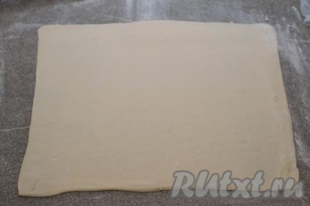 На стол, присыпанный мукой, выложить разморозившийся пласт слоёного теста, раскатать его скалкой в прямоугольник толщиной около 2 миллиметров. У меня получился прямоугольник размером 27 сантиметров на 33 сантиметра.