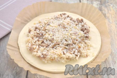 Отступая от краёв круга из слоёного теста по 2 сантиметра, выкладываем на тесто начинку из риса и фарша, разравниваем её.