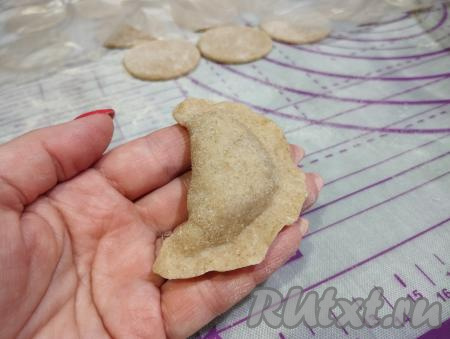 Соединяем края кружка над начинкой, формируя заготовку пельменя в виде полумесяца.